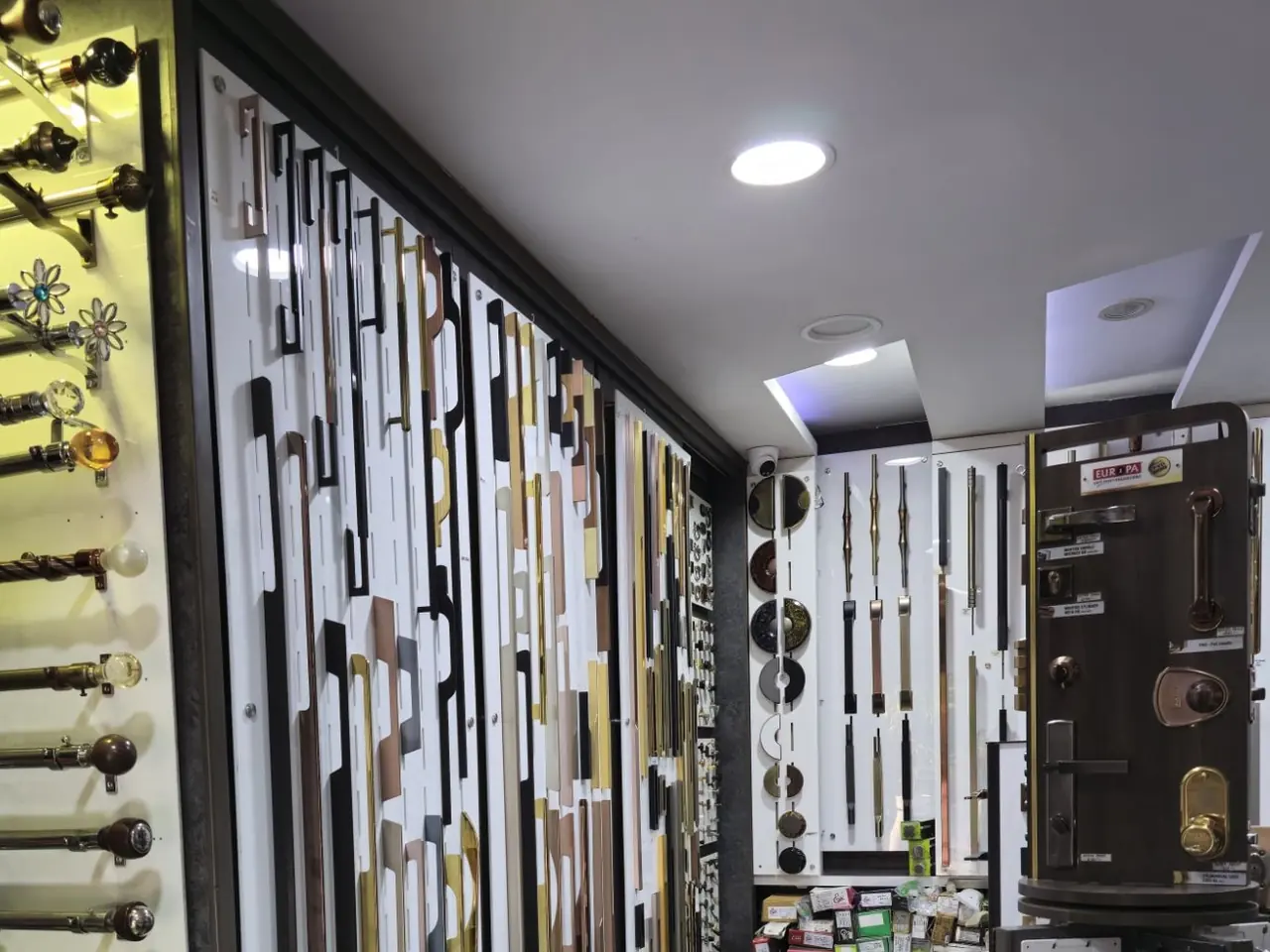 A wall of long handles in brass, black, copper and steel finishes, with curtain rods on the left and a lock display stand on the right