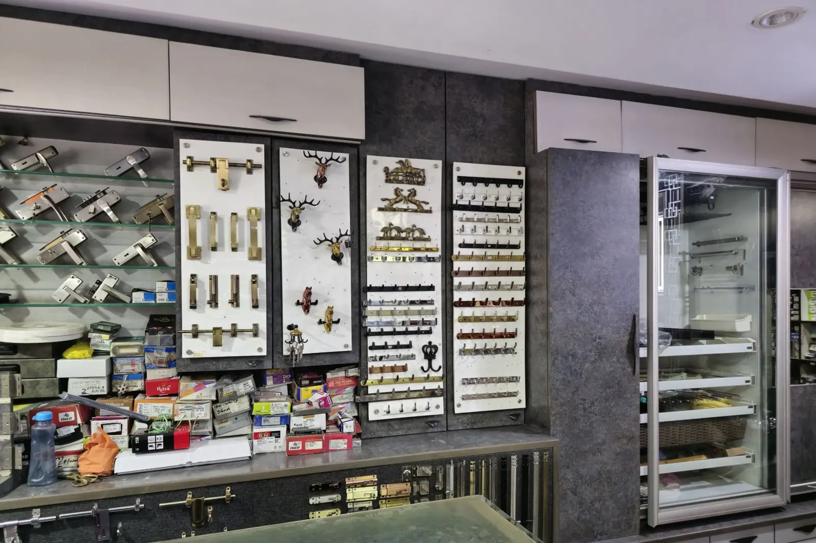 Inside the showroom: lever handles on glass shelves, brass aldrops and tower bolts, decorative wall hooks in several finishes and a tall pantry unit behind glass